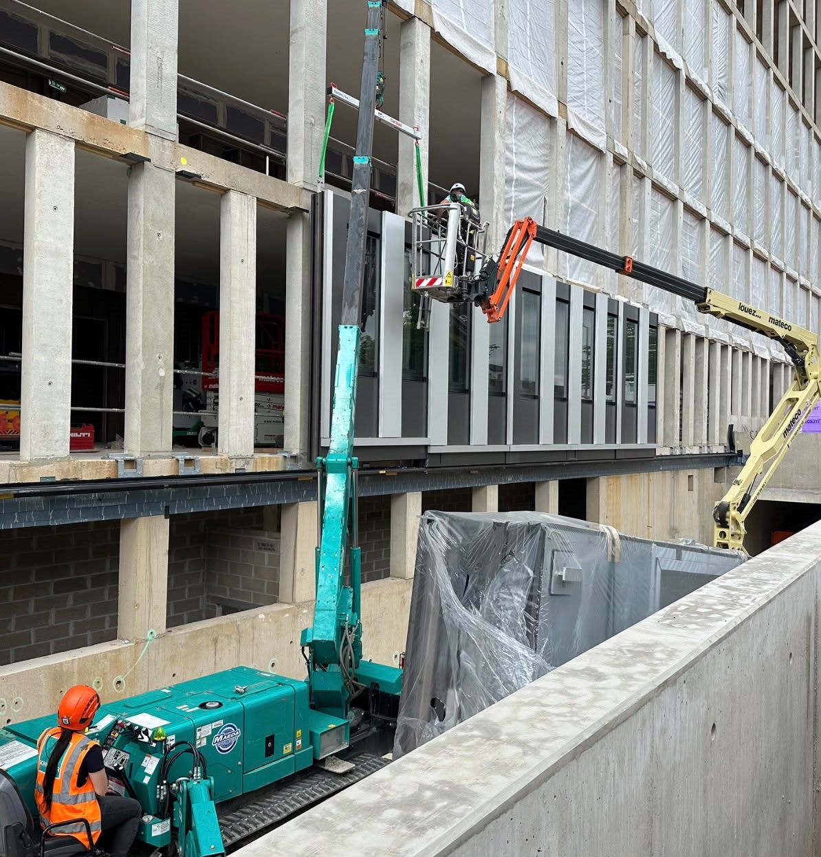 Crane positioning a large façade section between concrete floors