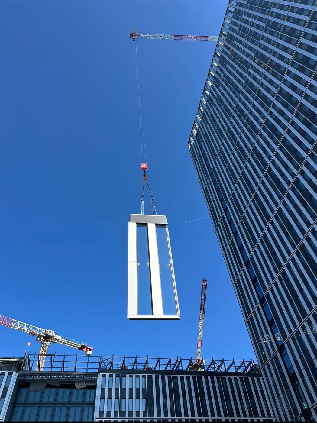 Tower crane lifting a tall unitised panel up a glazed tower